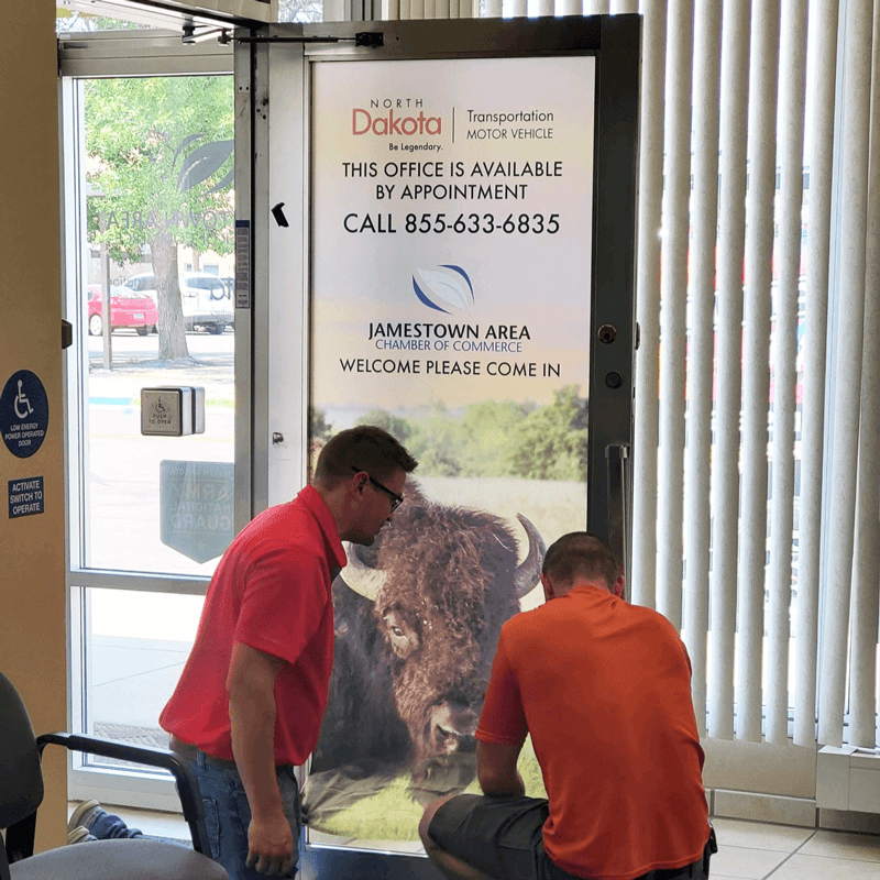Newman print team installing perforated window film on entry door.