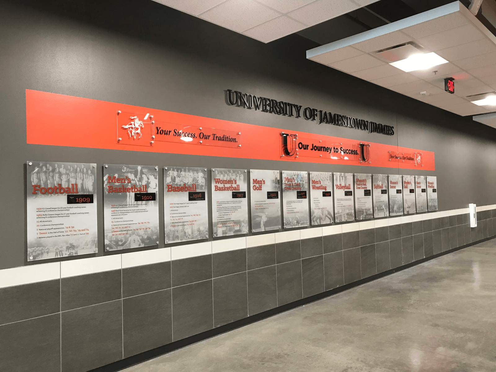 Wall with a long horizontal banner and framed documents in a hallway, featuring the University of Jamestown logo.