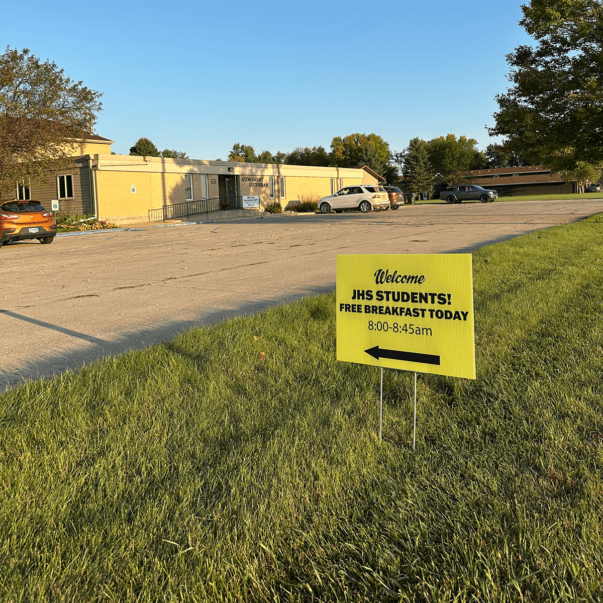 Yellow sign welcoming JHS students to free breakfast today on a grassy area near a church in Jamestown, ND.